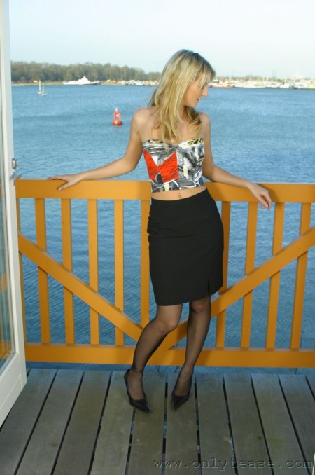 Playful blonde Jamie C in red garters and black stockings does some posing on balcony